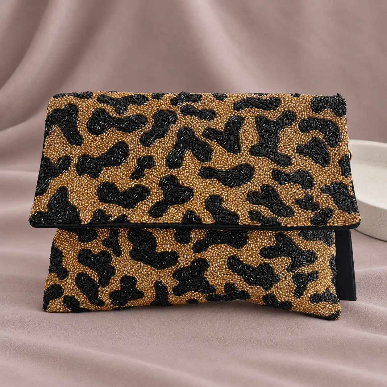 Tiger Beaded Clutch standing upright on muted mauve fabric with visible minimal white styling props