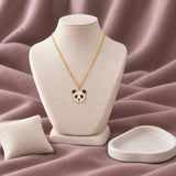 Panda Enamel Necklace — on an ivory display with mauve fabric and white styling props
