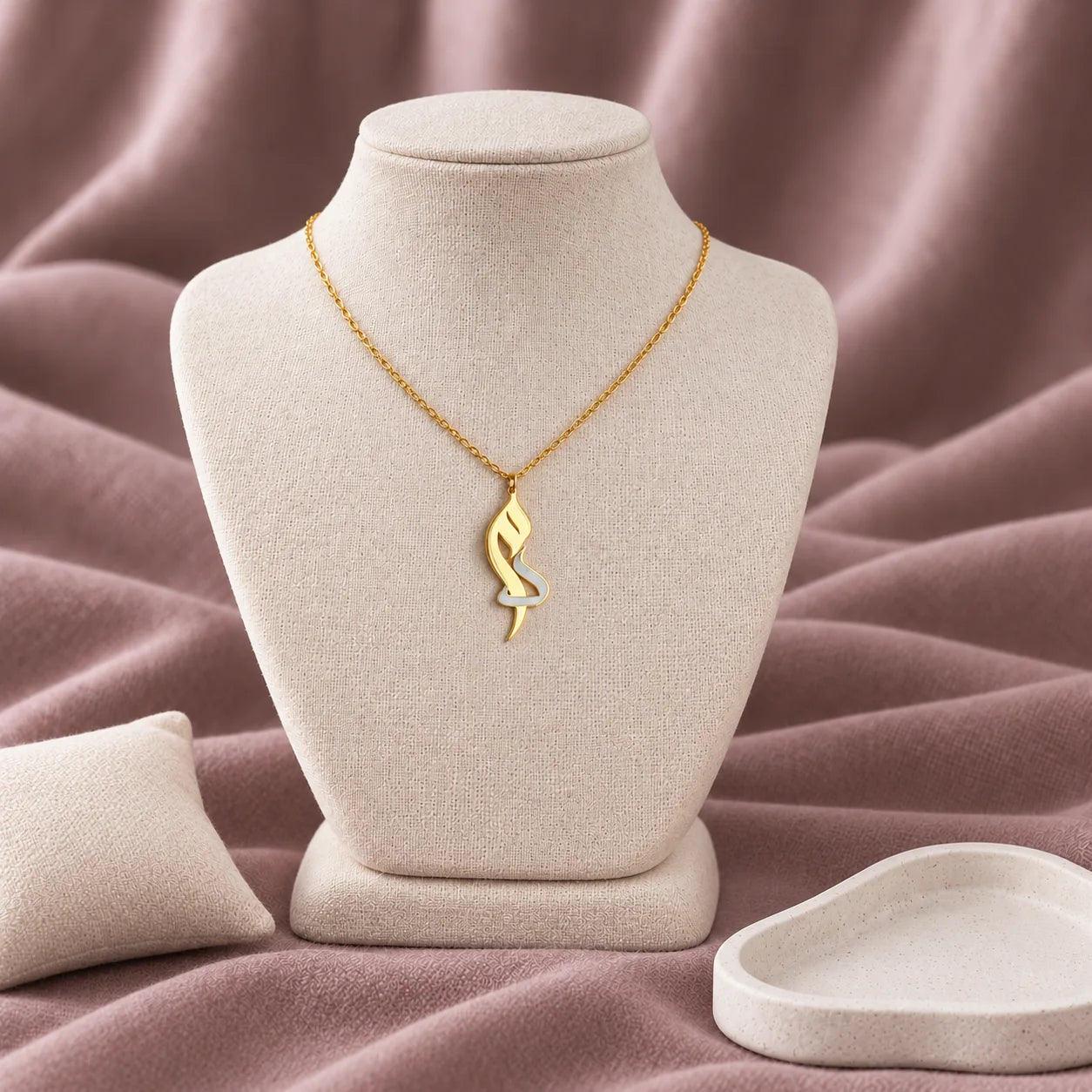Arabic Initial Enamel Necklace — on an ivory display with mauve fabric and white styling props
