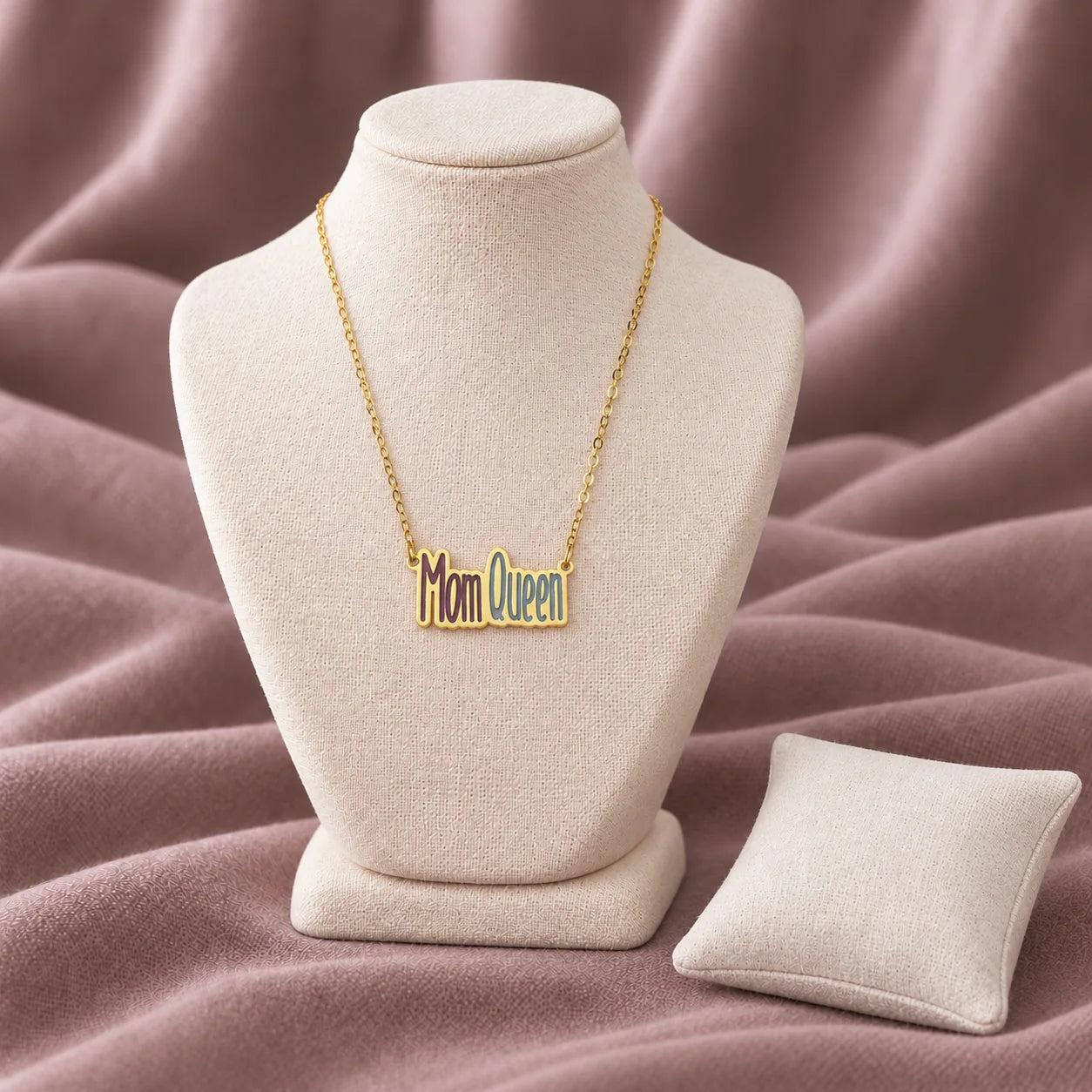 Mom Queen Enamel Necklace — on an ivory display with mauve fabric and white styling props