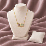 Mom Queen Enamel Necklace — on an ivory display with mauve fabric and white styling props