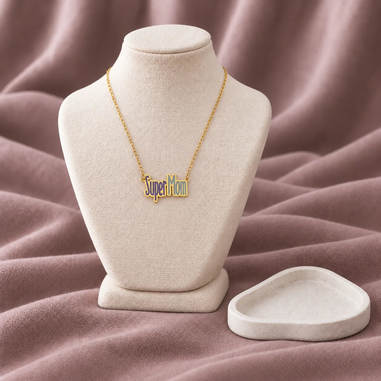 Super Mom Enamel Necklace — on an ivory display with mauve fabric and white styling props