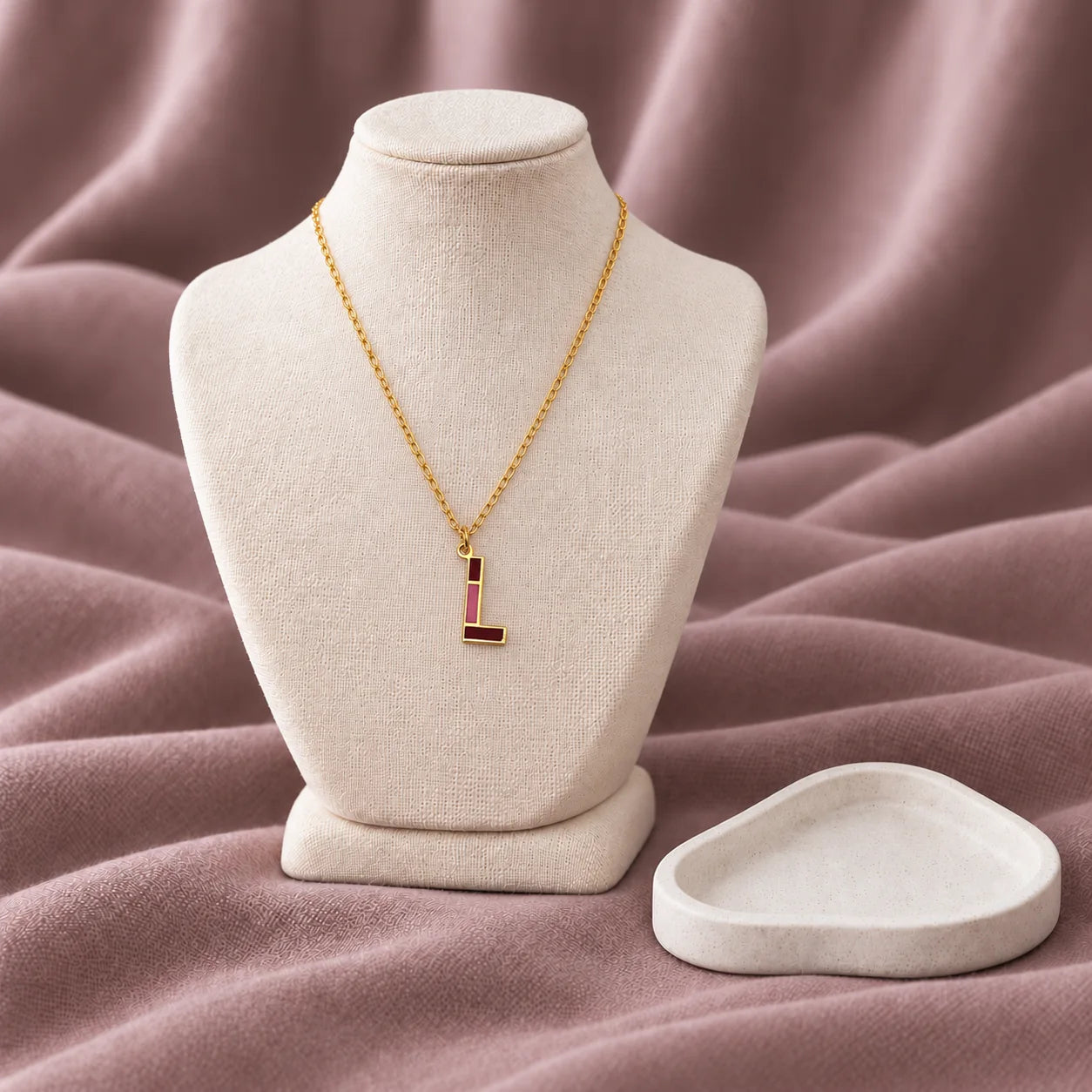 Enamel Initial Necklace — on an ivory display with mauve fabric and white styling props