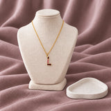 Enamel Initial Necklace — on an ivory display with mauve fabric and white styling props